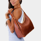 Nutmeg Medium | Model holding u-shaped, flat-bottomed leather shoulder bag with adjustable strap