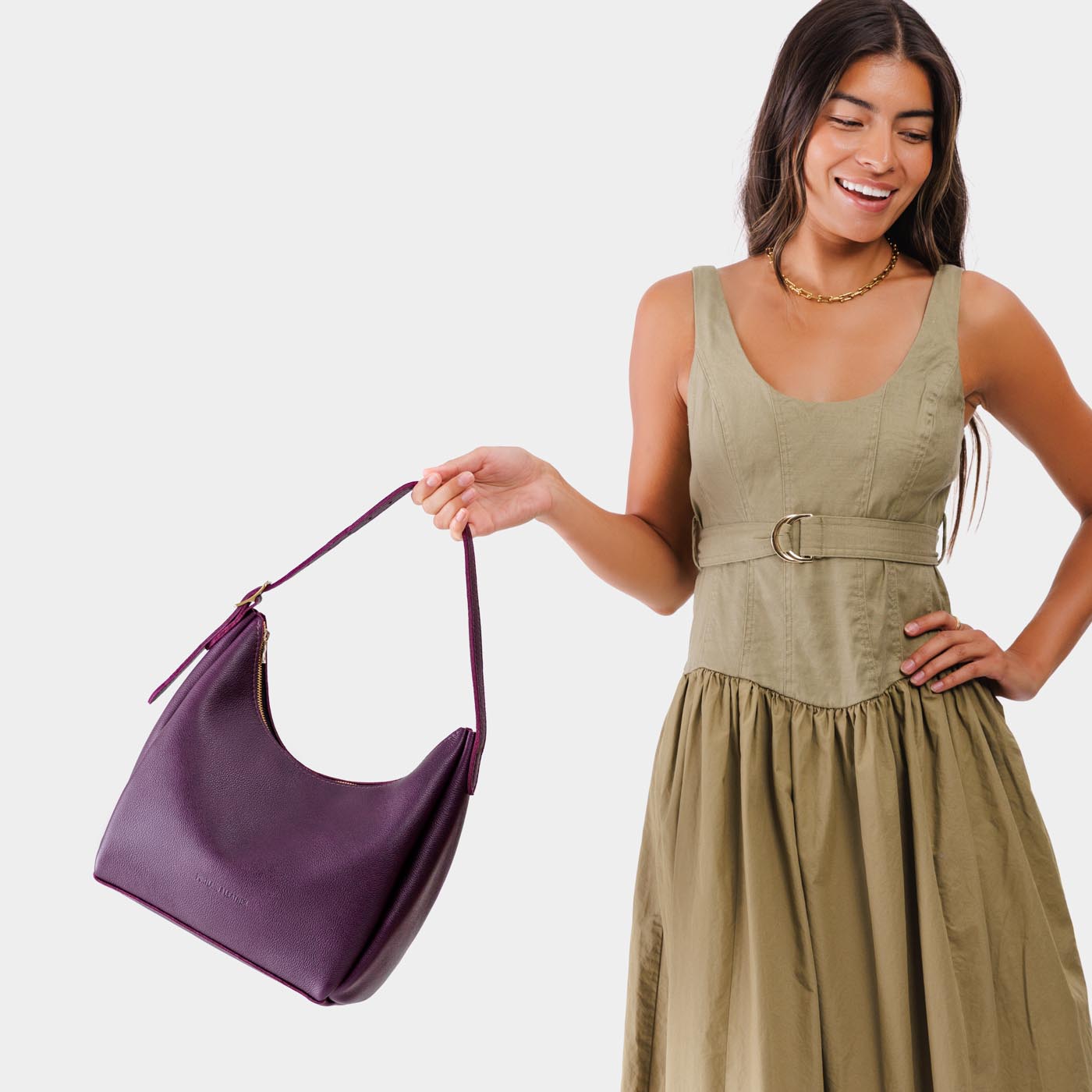 Plum*Medium | Model holding u-shaped, flat-bottomed leather shoulder bag with adjustable strap