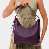 Plum Medium | Model holding u-shaped, flat-bottomed leather shoulder bag with adjustable strap