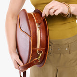 Nutmeg | Model carrying large circle shaped leather bag with top zipper and carrying strap