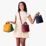 All Variants | A model holding several petite crossbody tote bags with zipper closures and front pockets