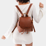 Nutmeg | Pebbled brown leather drawstring backpack being worn by a person wearing a white dress.