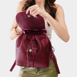 Orchid | Pebbled burgundy leather drawstring backpack being held by a person.