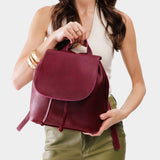 Orchid | Pebbled burgundy leather drawstring backpack being held by a person.