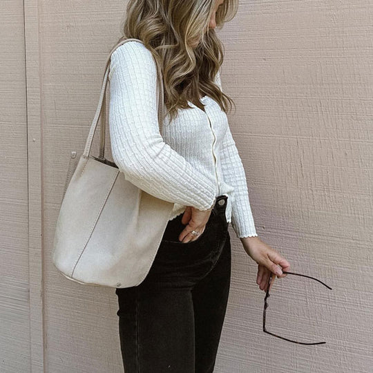 A person holding a Devan Bucket Tote, standing in front of a taupe wall.