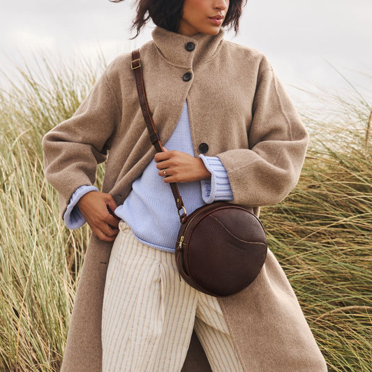A model standing on the beach wearing a Coldbrew Circle Crossbody bag.