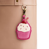 Wild Rose | A cupcake-shaped leather keychain charm with cream-colored frosting, a red cherry on top hanging on a bag