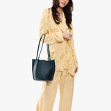 Boreal Classic | Model wearing matching light yellow shirt and trousers carrying petite bucket shaped tote bag with matching leather handles
