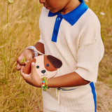 All Variants | A child in a field holding a dog shaped leather pouch with embroidered facial details and a wrist strap.