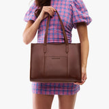 Cognac East/West | Model holding structured wide tote bag with overlapping panels and crossbody strap