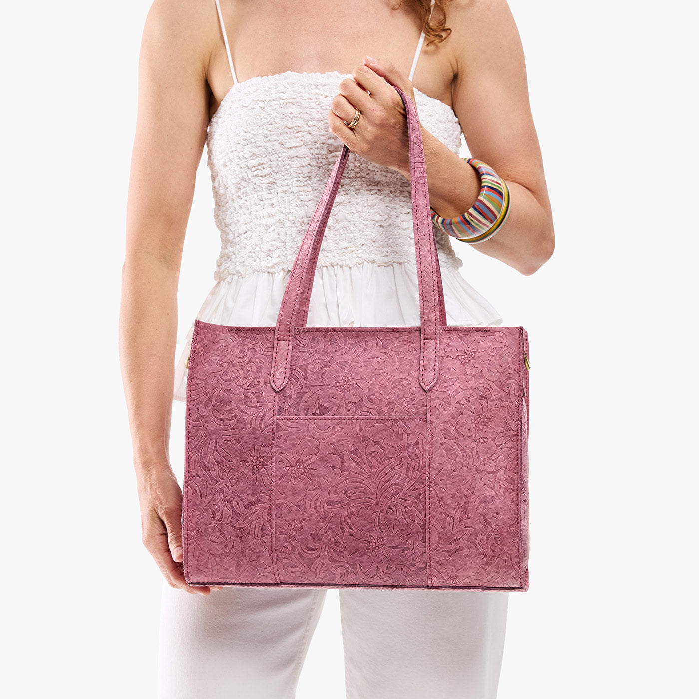 Hollyhock | Model holding structured wide embossed leather tote bag with overlapping panels and crossbody strap