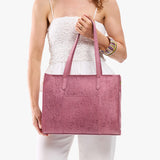 Hollyhock | Model holding structured wide embossed leather tote bag with overlapping panels and crossbody strap
