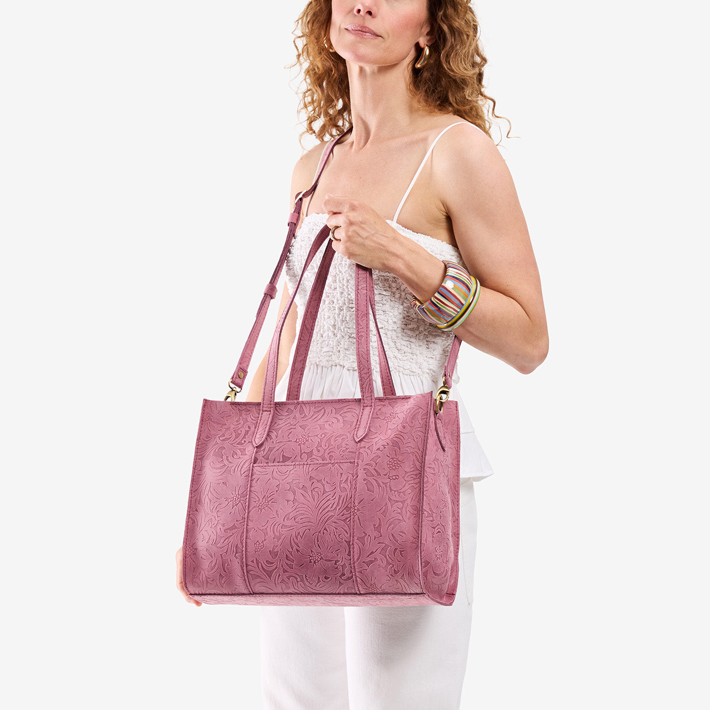 Hollyhock | Model holding structured wide embossed leather tote bag with overlapping panels and crossbody strap