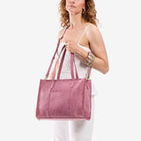 Hollyhock | Model holding structured wide embossed leather tote bag with overlapping panels and crossbody strap