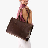 Chocolate Brown Oversized East/West | Model holding structured wide tote bag with overlapping panels and crossbody strap