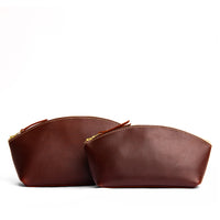 Cognac | Size comparison shot of two spacious leather makeup bags with curved seams and top zipper