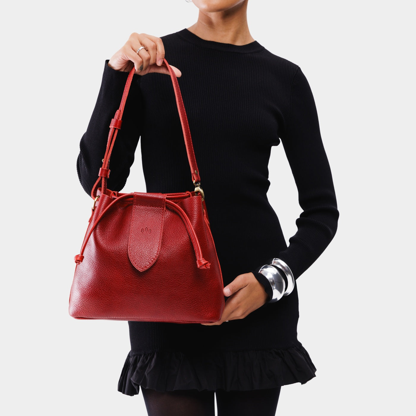 Chili Red*Large | Model holding symmetrical leather bag with leather drawstring closure and adjustable shoulder strap