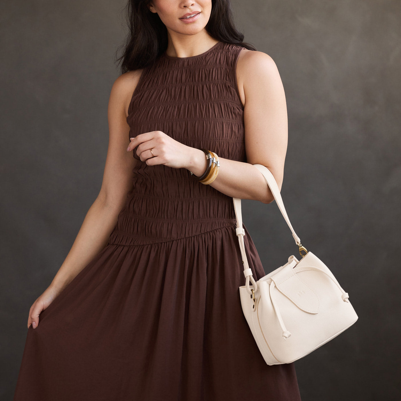 Pebbled Bone*Small | Model holding symmetrical leather bag with leather drawstring closure and adjustable shoulder strap