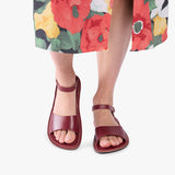 Marsala | Close-up of a person wearing colorful dress and red flat sandals with an ankle strap and buckle, shown against a plain background.