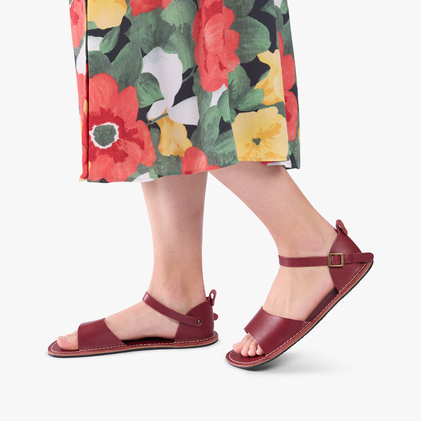 Marsala | Close-up of a person wearing colorful dress and red flat sandals with an ankle strap and buckle, shown against a plain background.