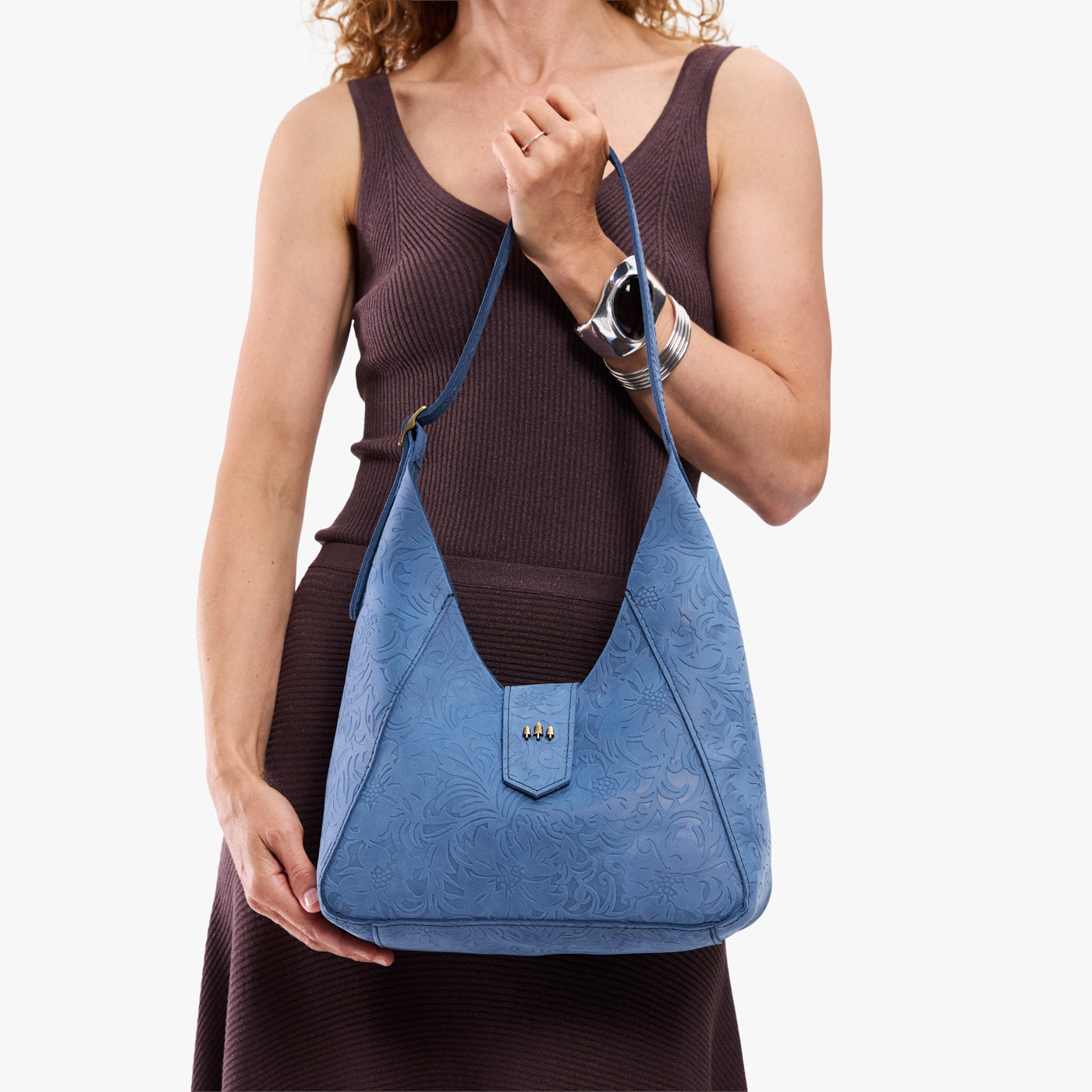 Cornflower | Model carrying structured hobo shoulder bag with floral patterned embossed leather, adjustable strap and magnetic closure