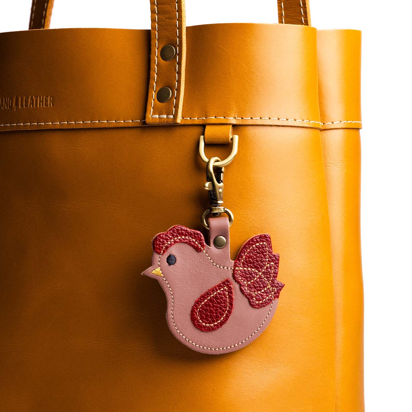 Francesca | Pink chicken-shaped keychain attached to a D-ring on a yellow leather bag.