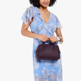 Larkspur Large | A large bowler styled bag with a crossbody strap being held by a model in a light blue floral dress