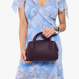 Larkspur Large | A large bowler styled bag with a crossbody strap being held by a model in a light blue floral dress