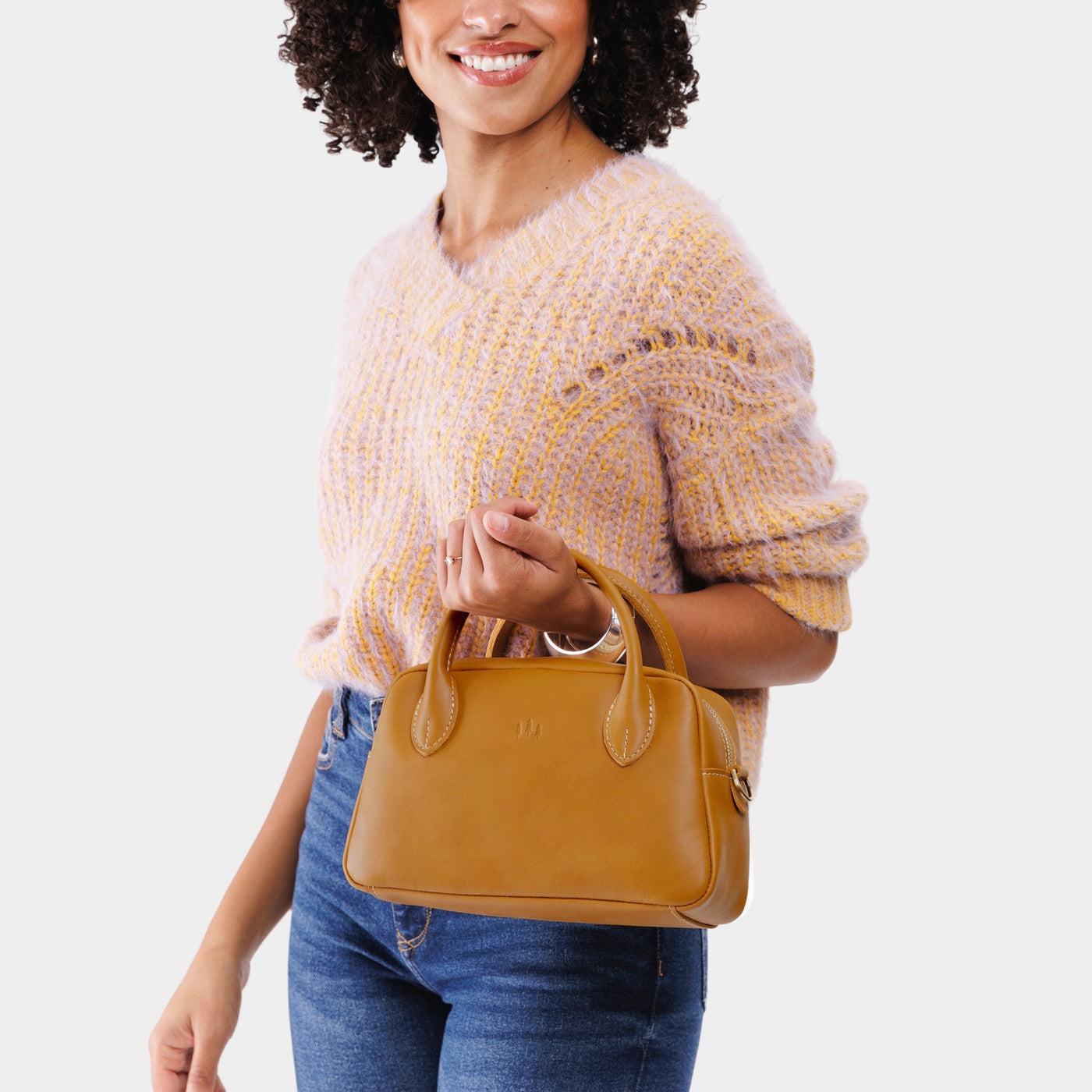 Mango*Large | A large bowler styled bag with a crossbody strap being held by a model wearing a knit sweater and jeans