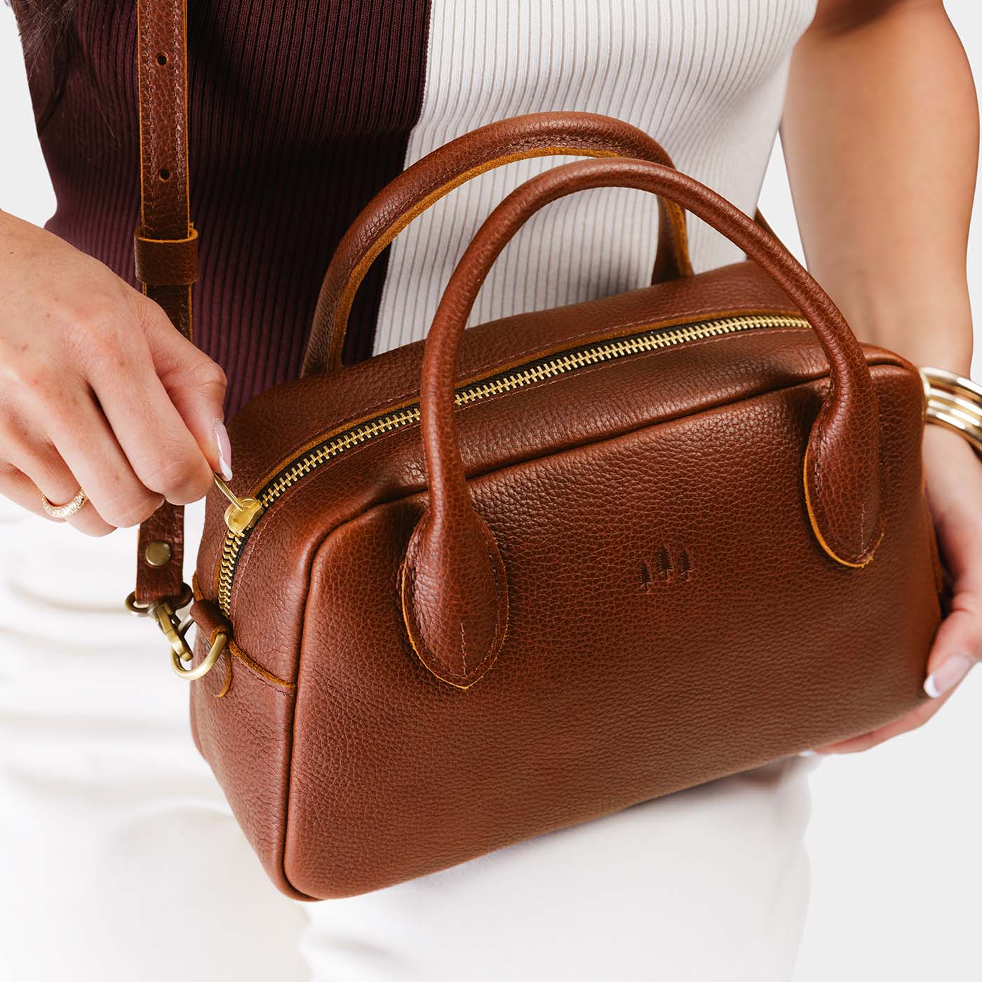Nutmeg*Large | A bowler styled bag with a crossbody strap being held by a model wearing a brown and white top