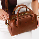 Nutmeg Large | A bowler styled bag with a crossbody strap being held by a model wearing a brown and white top