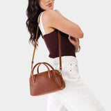Nutmeg Large | A bowler styled bag with a crossbody strap being worn by a model wearing a brown and white top