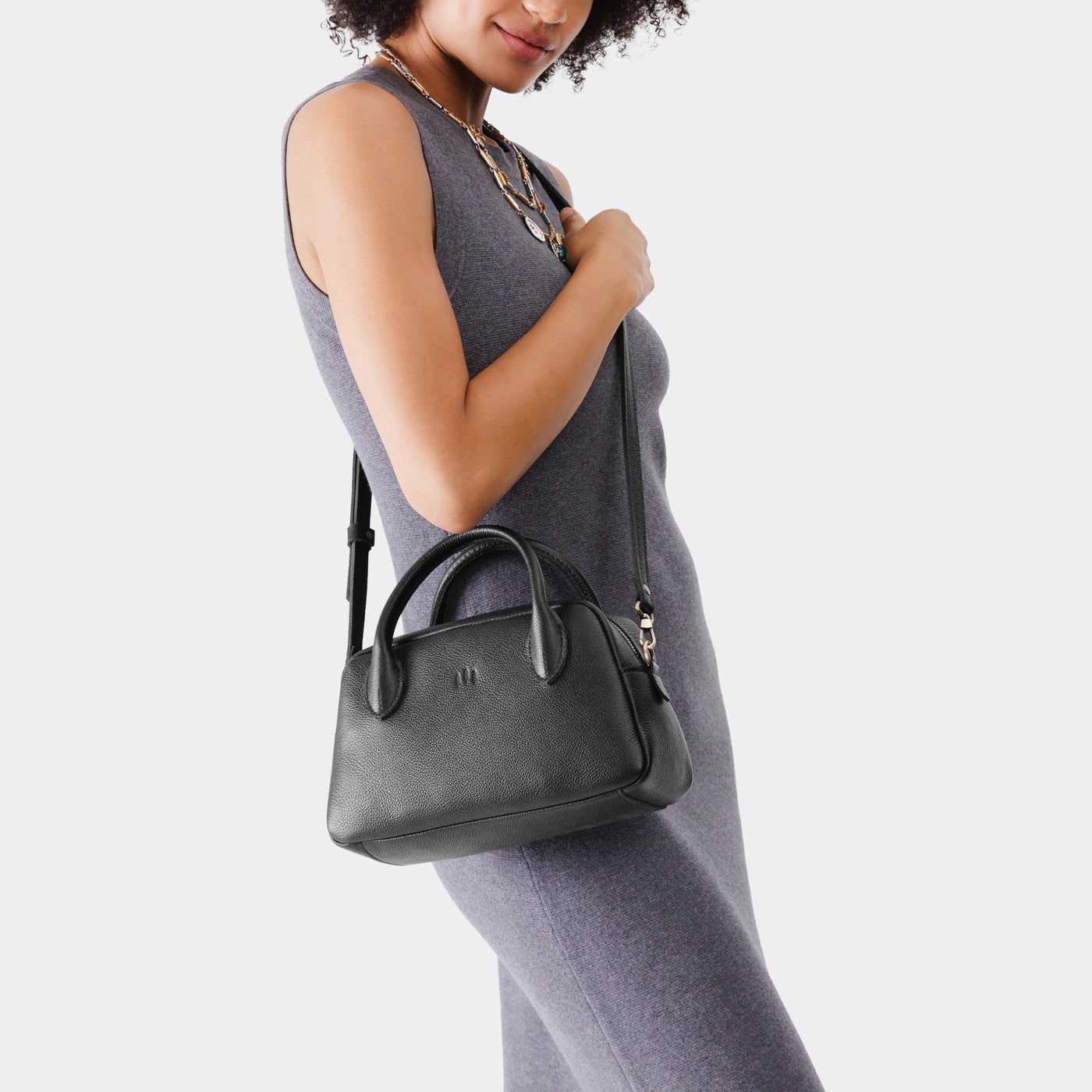 Pebbled--black*Large | A bowler styled bag with a crossbody strap being held by a model wearing a dress