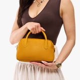 Sunshine Large | A large bowler styled bag with a crossbody strap being held by a model in a neutral outfit