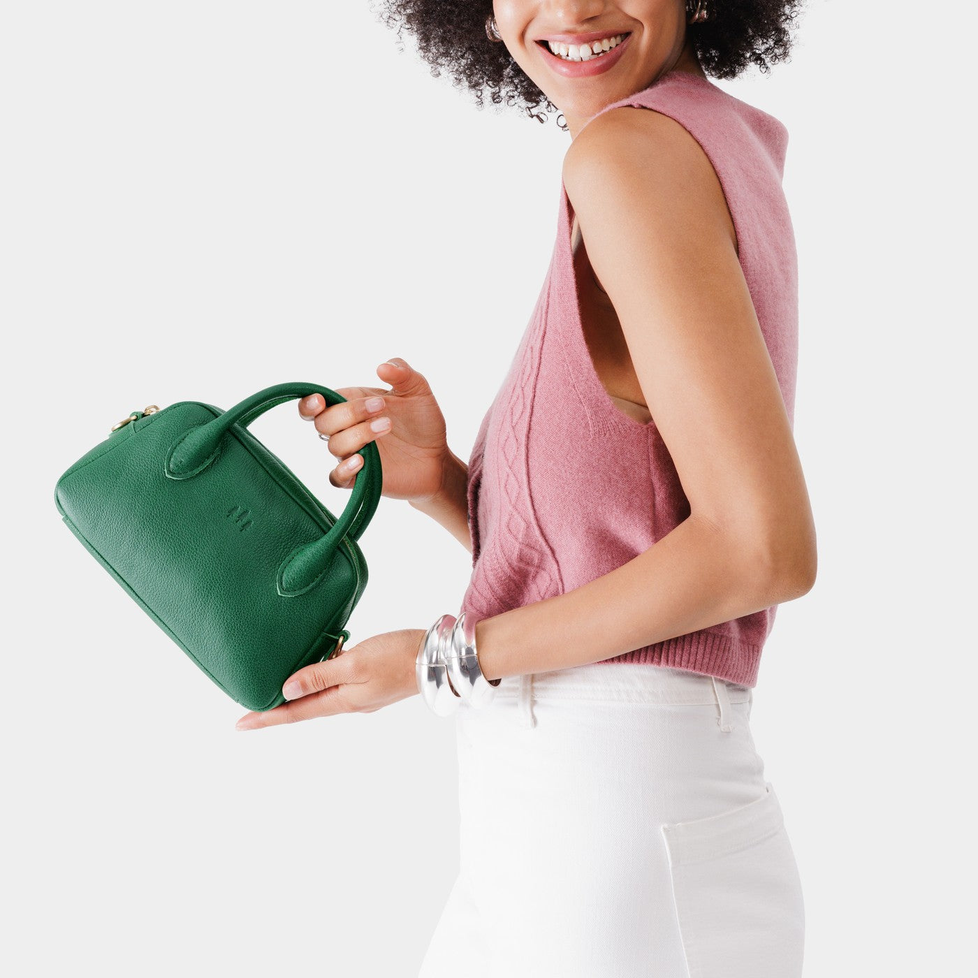 Bacalar*Small | A bowler styled bag with a crossbody strap being held by a model wearing a pink knit vest