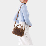 Canyon Small | A bowler styled bag with a crossbody strap being worn by a model wearing a light blue sweater