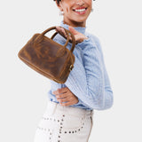 Canyon Small | A bowler styled bag with a crossbody strap being held by a model wearing a light blue sweater