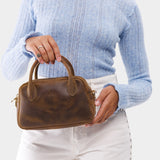 Canyon Small | A bowler styled bag with a crossbody strap being held by a model wearing a light blue sweater