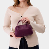 Lollipop Small | A bowler styled bag with a crossbody strap being worn by a model wearing a taupe top