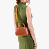 Sienna Small | A bowler styled bag with a crossbody strap being held by a model wearing a dress