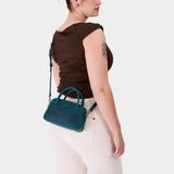 Westward Blue Small | A bowler styled bag with a crossbody strap being worn by a model in a brown shirt 