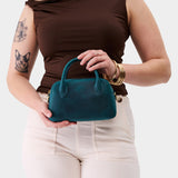  Westward Blue Small | Bowler styled bag with a crossbody strap being held by a model in a brown shirt 