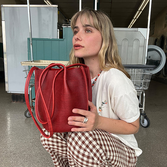 A woman crouching in a store while holding a red leather bucket bag