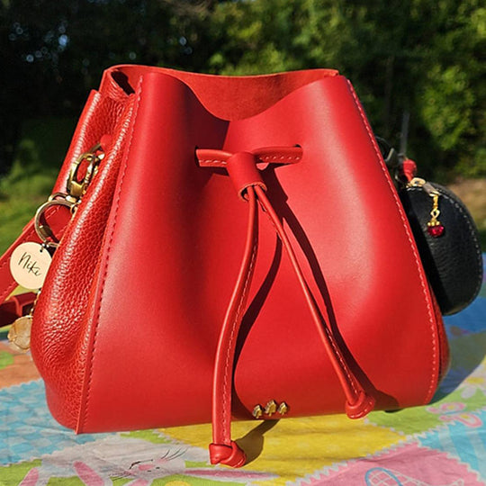 A bright red pebbled leather bucket bag outdoors on a colorful surface with green foliage in the background