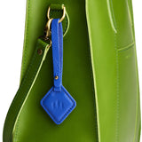 Astro Blue | Rhombus-shaped leather tag with a strap and debossed PLG design hanging from a green leather bag