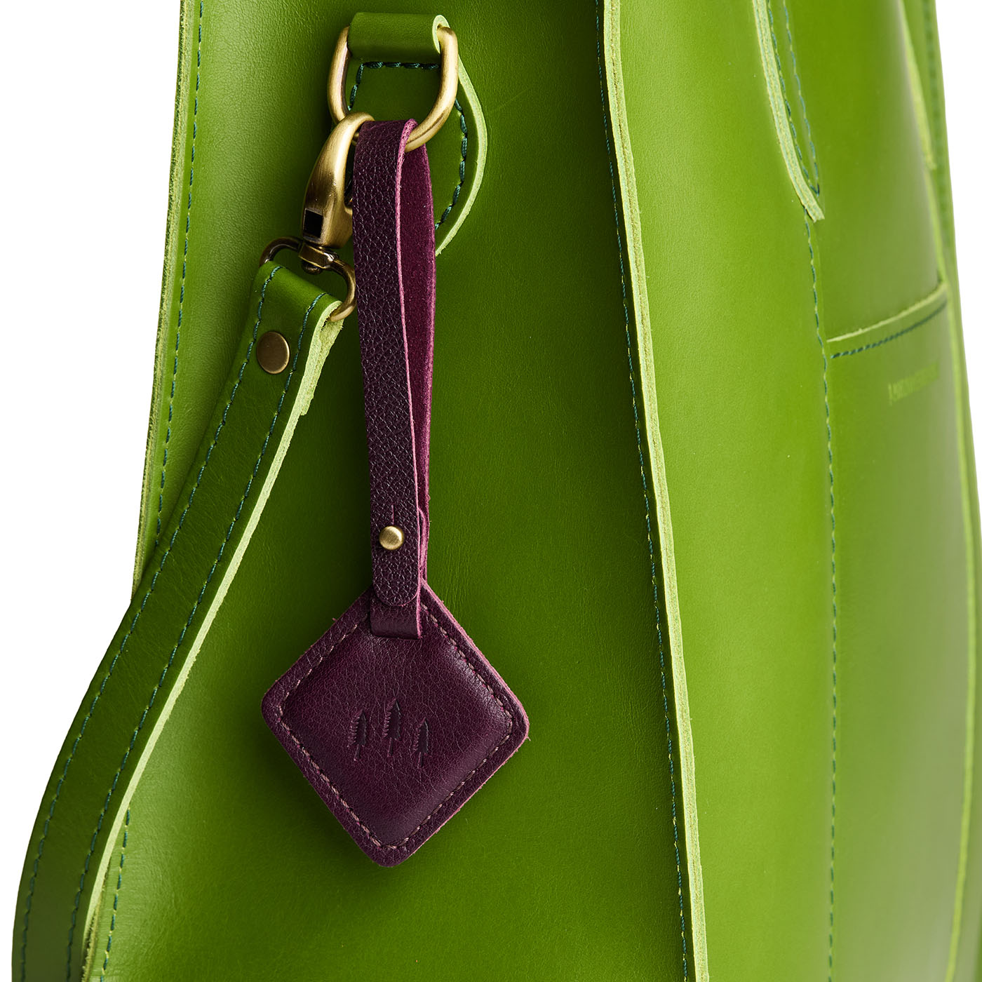 Plum | Rhombus-shaped leather tag with a strap and debossed PLG design hanging from a green leather bag