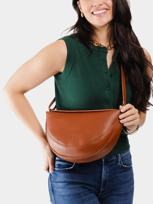 Model wearing half circle shaped leather sling bag in honey