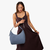 Denim Large | Model holding u-shaped, flat-bottomed leather shoulder bag with adjustable strap