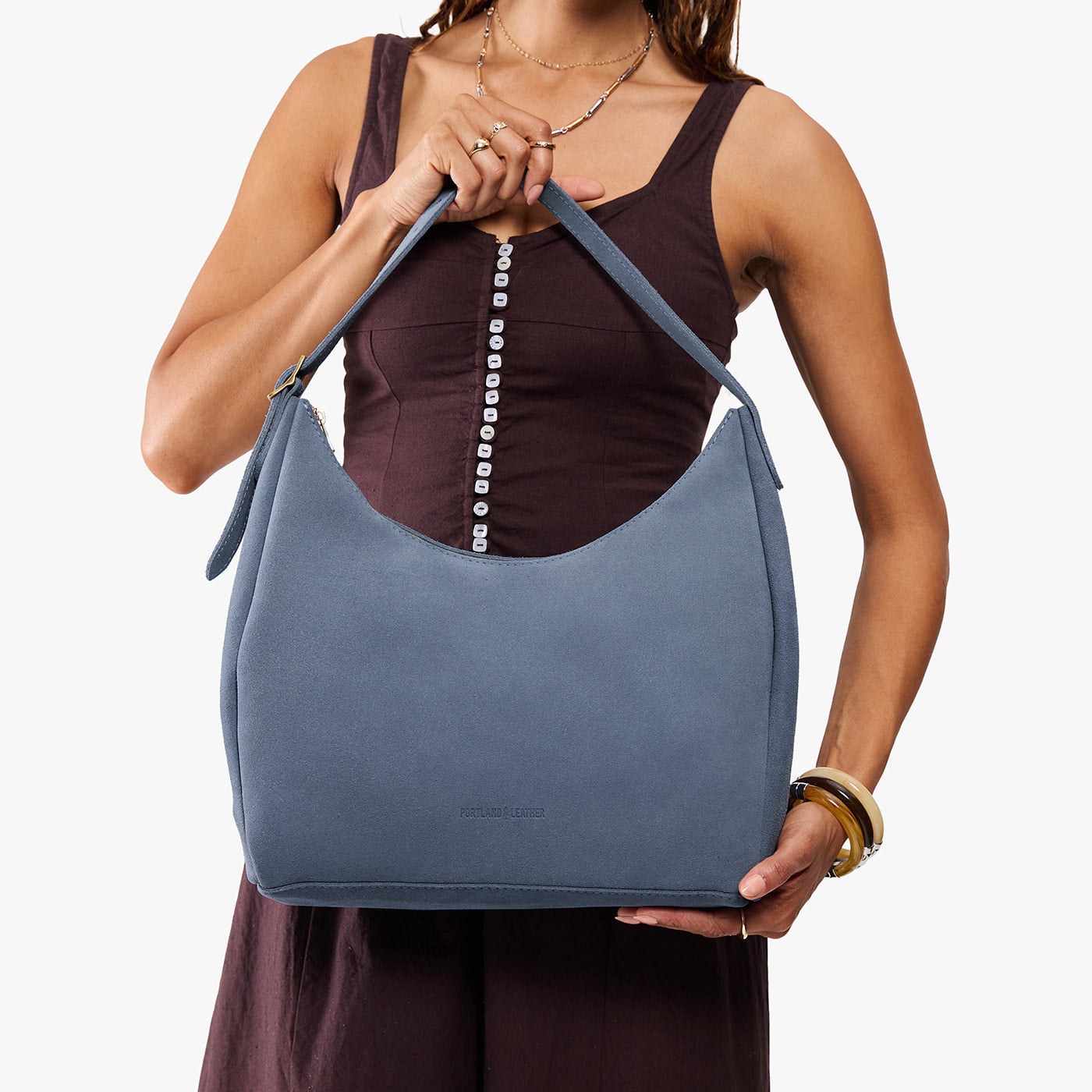 Denim*Large | Model holding u-shaped, flat-bottomed leather shoulder bag with adjustable strap