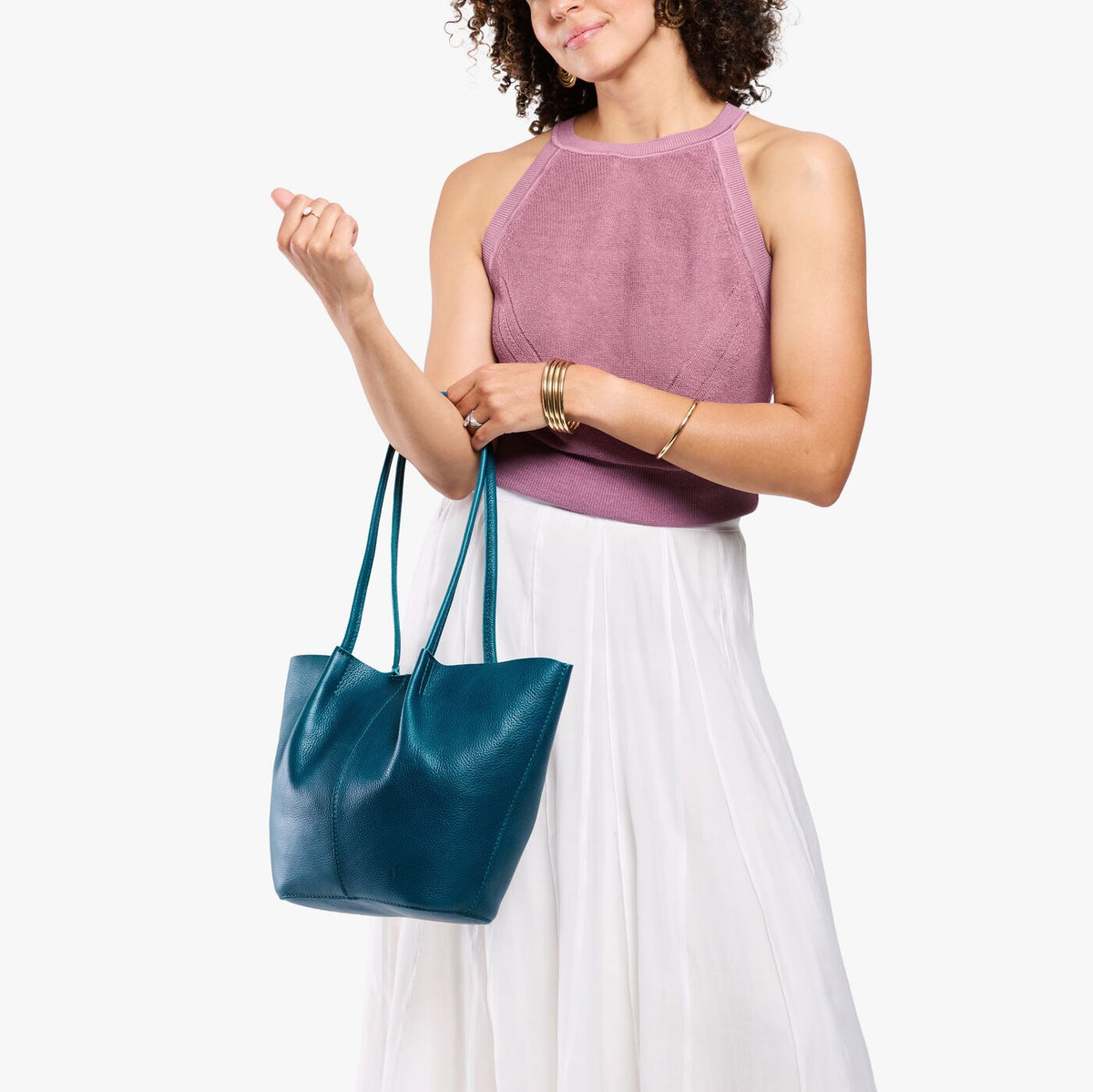 Model wearing mauve sleeveless top, white skirt, and gold wrist bangles carrying Large Devan Bucket Tote in Planetary